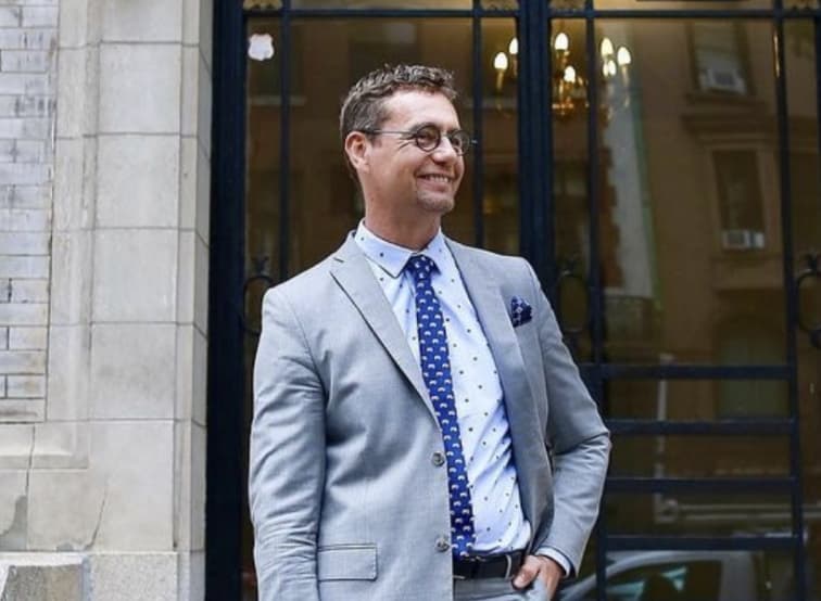 Dr. Konstantin posing in front of building wearing a gray suit