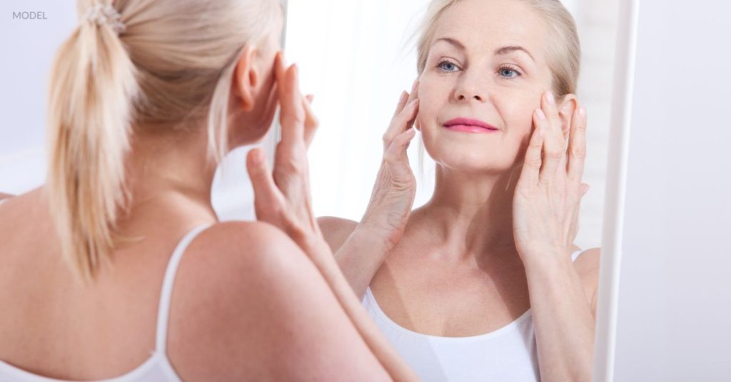 Woman (model) looks at her face in the mirror and smiles.