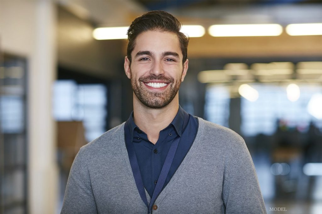 Man wearing a cardigan and smiling in an office building (MODEL)
